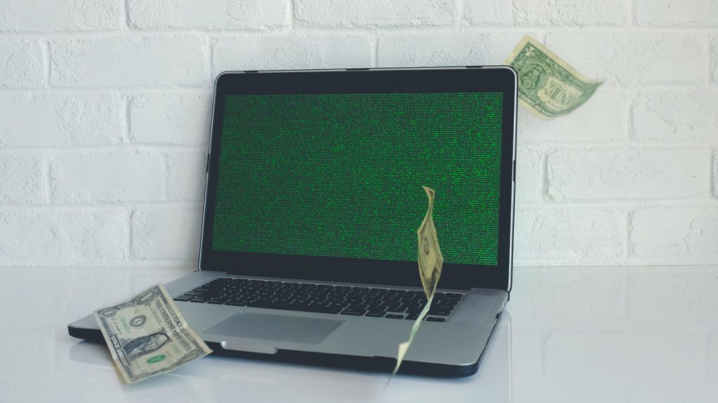 Laptop mit grünen Zahlen, die über den Display rauschen, und Geldscheinen, die auf den Laptop herunterrieseln.