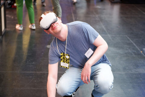 Zu sehen ist ein junger Mann, der eine VR-Brille trägt und auf dem Boden kniet.