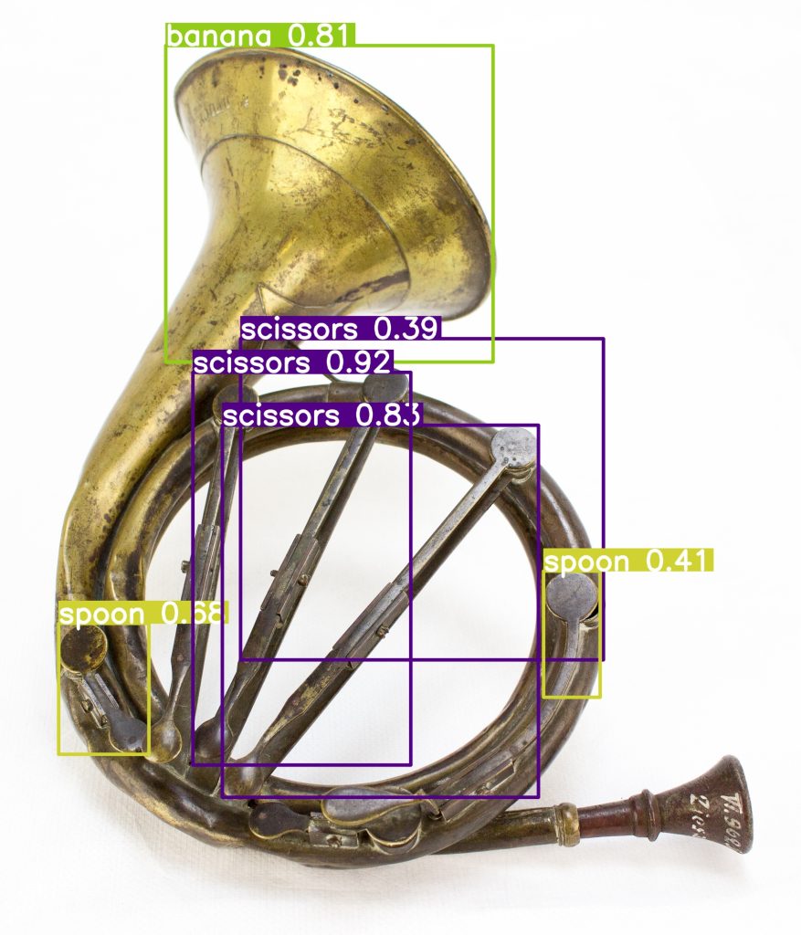 Klappenhorn (Metall-Blasinstrument) aus Messing, zweiwindig, mit 6 Klappen. Um zwei der Klappen herum befinden sich rechteckige Rahmen mit dem Schlagwort "spoon". Drei weitere Elemente des Horns werden als "scissors" erkannt, der Schalltrichter als Banane - mit einem "confidence"-wert von 81 Prozent.