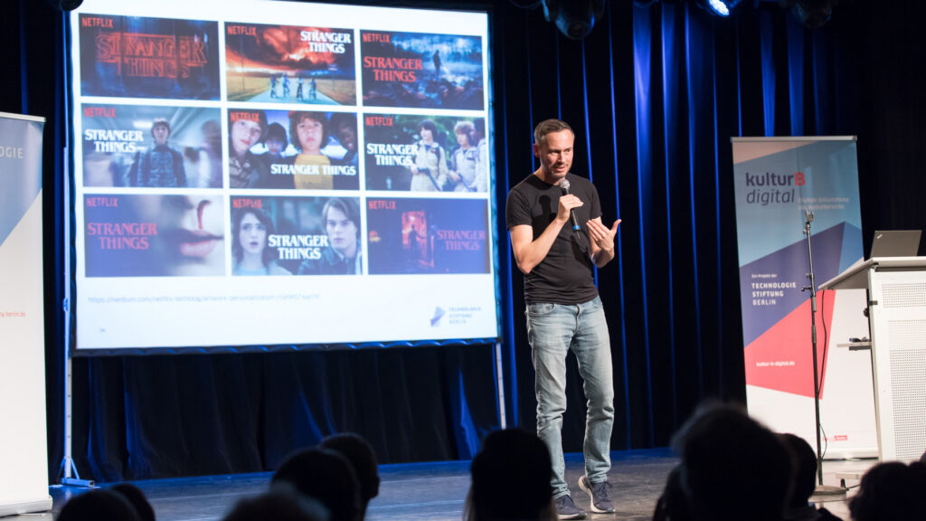 Nicolas Zimmer auf der Bühne vor einer Präsentation mit Werbetafeln der Streaming-Plattform Netflix.