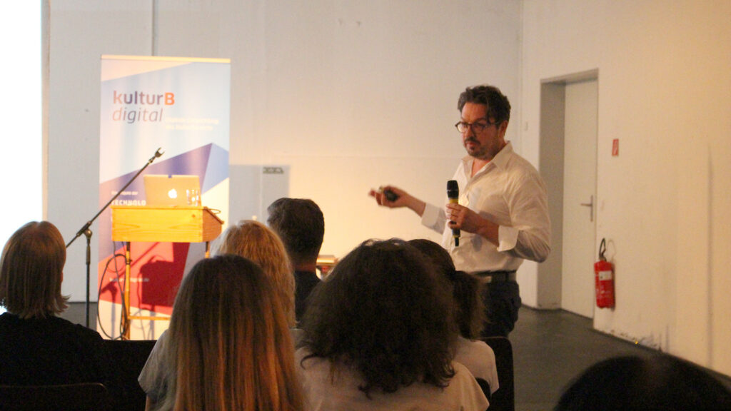 Dr. Martin Tröndle spricht vor sitzendem Publikum. Im Hintergrund: Banner von kulturBdigital.