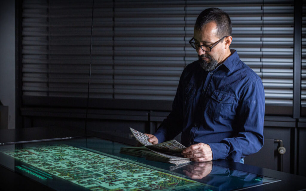Interface Designer Edmundo Galindo steht vor einem Medientisch, der einen Ausschnitt aus einer Bildhandschrift zeigt. In seinen Händen: eine physische Replik.
