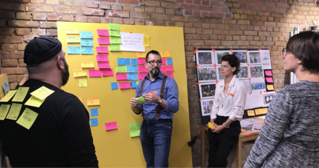 Interface-Designer Edmundo Galindo und Mitarbeitende des Berliner Ensembles sammeln auf farbigen Klebezetteln Ideen. Einer Person kleben einige Zettel am Rücken.