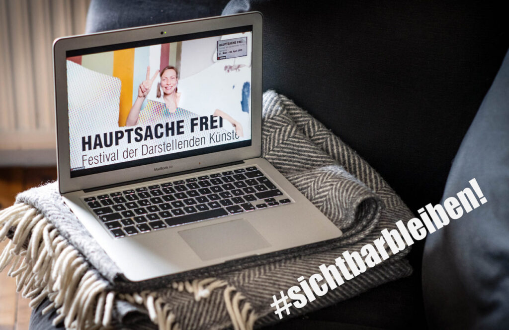 Titelbild des Hauptsache Frei Festivals auf einem Laptop, der aufgeklappt auf einer Wolldecke steht.