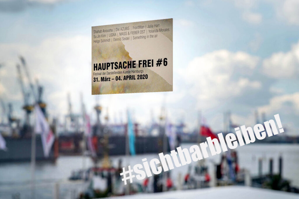 Eine Postkarte des Hauptsache Frei Festivals hängt an einer Glasscheibe. Darunter der Hashtag "sichtbarbleiben". Im Hintergrund: Schiffe im Hamburger Hafen.