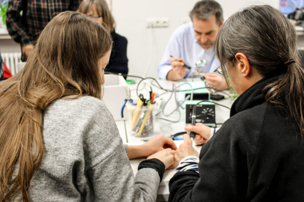 Besucher:innen in der Offenen Werkstatt der Technologiestiftung im CityLab löten Bauteile zusammen.