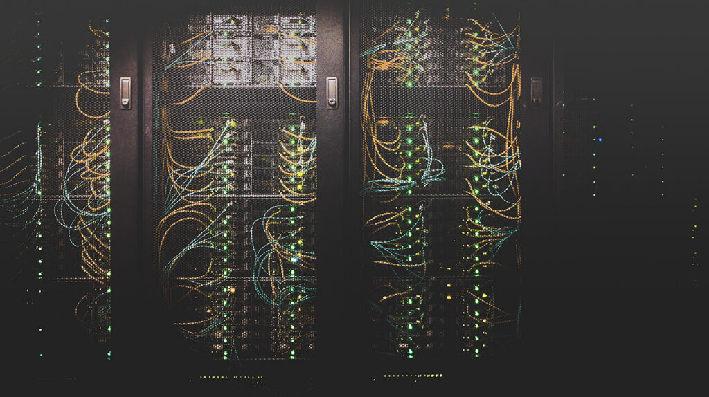Blick in einen dunklen Serverraum mit grün leuchtenden Server-Lämpchen und wilder Verkabelung.
