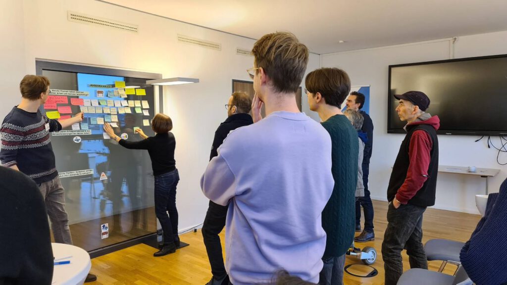 Bei einem Meeting betrachten Resilienz-Dispatcher:innen stehend Klebezettel mit Themen, die sie im letzten Jahr beschäftigt haben.