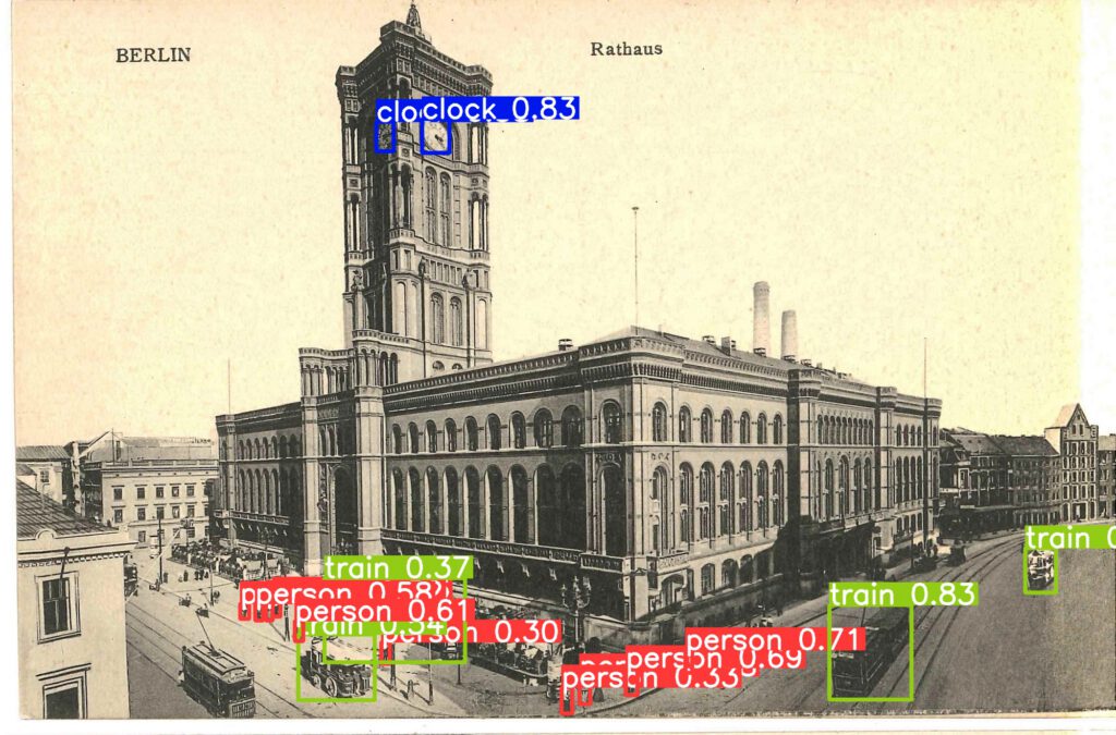 Ansichtskarte zeig das Rote Rathaus in Berlin. Elektrische Straßenbahnen und Pferdekutschen prägen das Straßenbild. Vor dem Rathaus sind Tische und Stühle aufgestellt, der Ratskeller wartet auf Gäste. Um vier Straßenbahnen herum befinden sich rechteckige Rahmen mit dem Schlagwort "train" und confidence-Werten von 34 bis 83 Prozent. Um die Turmuhr des Roten Rathauses befindet sich ein rechteckiger Rahmen mit dem Schlagwort "clock" und der Fundwahrscheinlichkeit von 83 Prozent. Auch sehr viele abgebildete menschen werden korrekt als "person" erkannt.