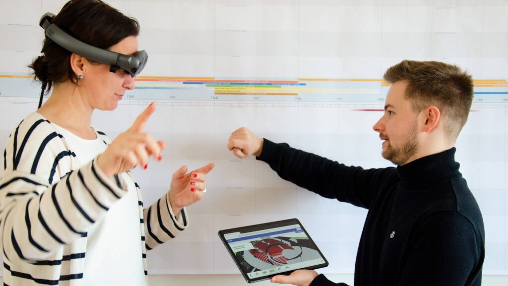 Frau mit Mixed-Reality-Brille steht einem Mann mit Tablet-Computer gegenüber, das einen Theatersaal als 3D-Modell zeigt.