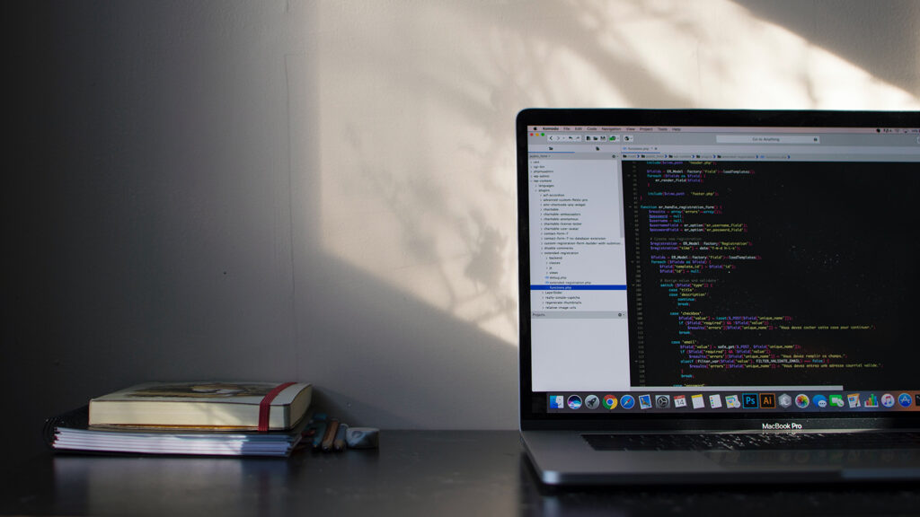 Ein geöffneter Laptop zeigt Quellcode. Neben dem Computer liegen Bücher.