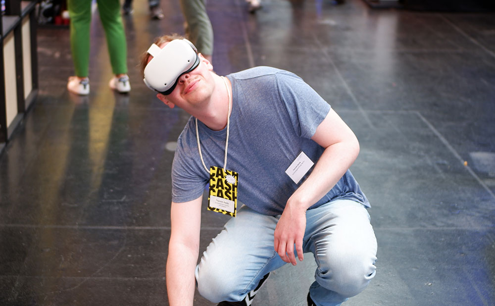 Ein junger Mann trägt eine VR-Brille auf dem Kopf und kniet auf dem Boden.