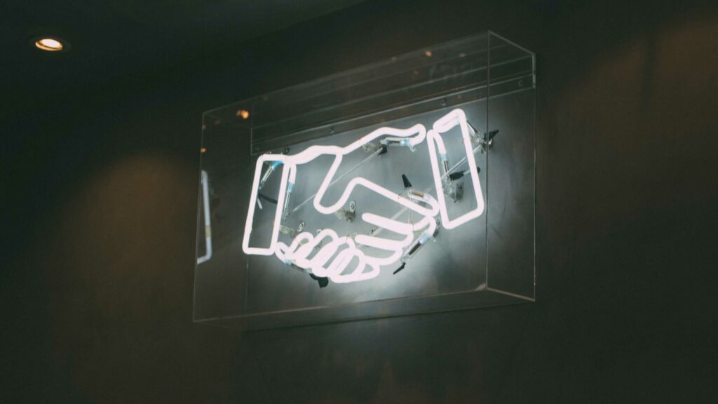 Neonschild an einer Wand in Form zweier zum Händedruck vereinter Hände.