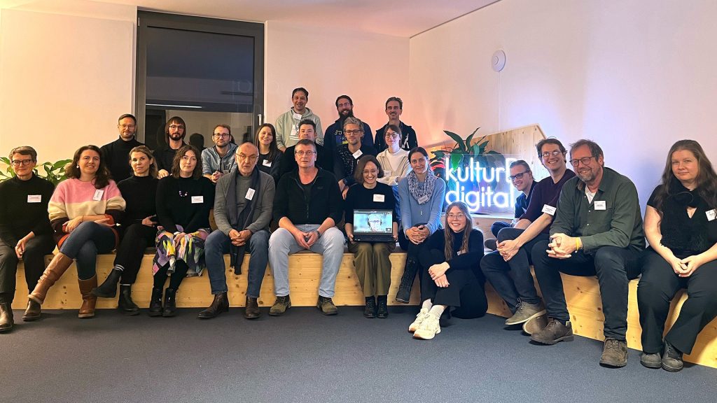 Eine Gruppe Personen - die Resilienz-Dispatcher:innen - sitzt gemeinsam mit dem kulturBdigital-Team auf einem Holzpodest.