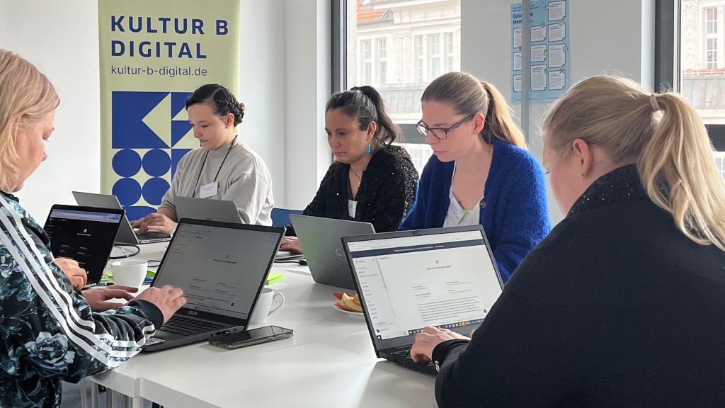 Fünf Teilnehmerinnen eines Workshops sitzen an einem Tisch, jeweils konzentriert an Laptops arbeitendend.