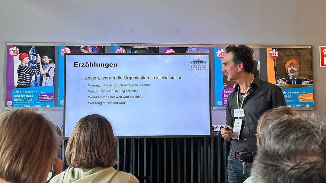 Holger Kral hält einen Vortrag im Foyer des ATZE Musiktheater. Die aktuelle Folie seiner Präsentation trägt den Titel "Erzählungen".