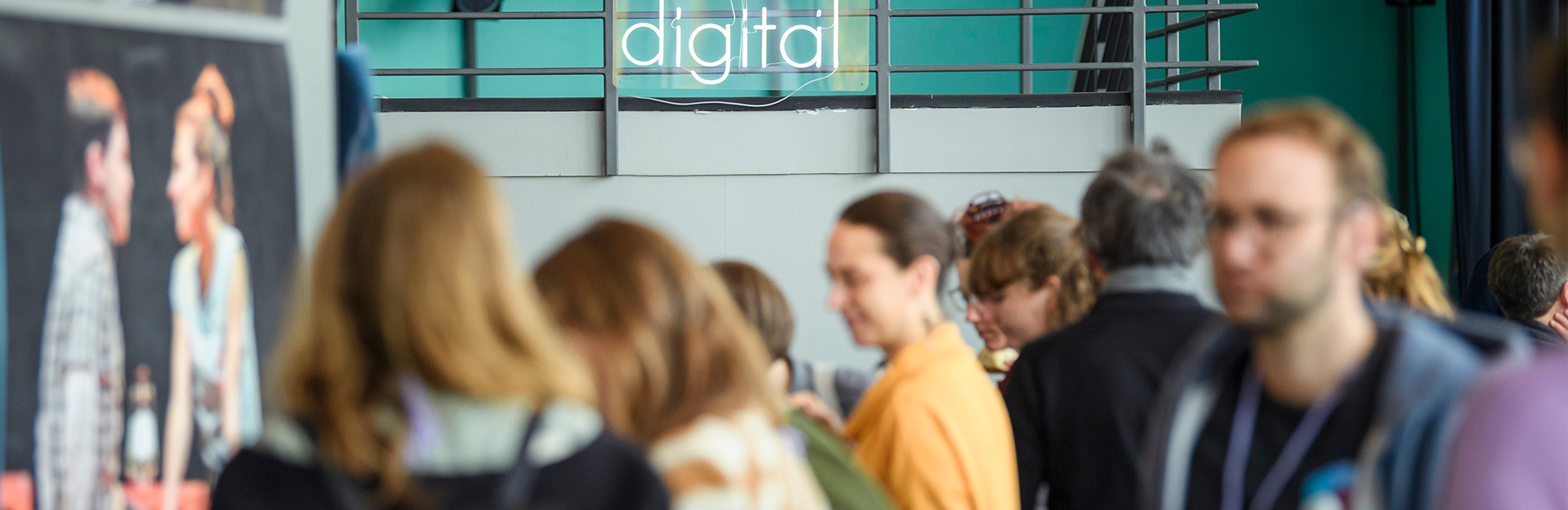 Gäste der kulturBdigital-Konferenz im Gespräch im Foyer eines Theaters, im Hintergrund hängt ein Neonschild mit der Aufschrift kulturBdigital an einem Geländer.
