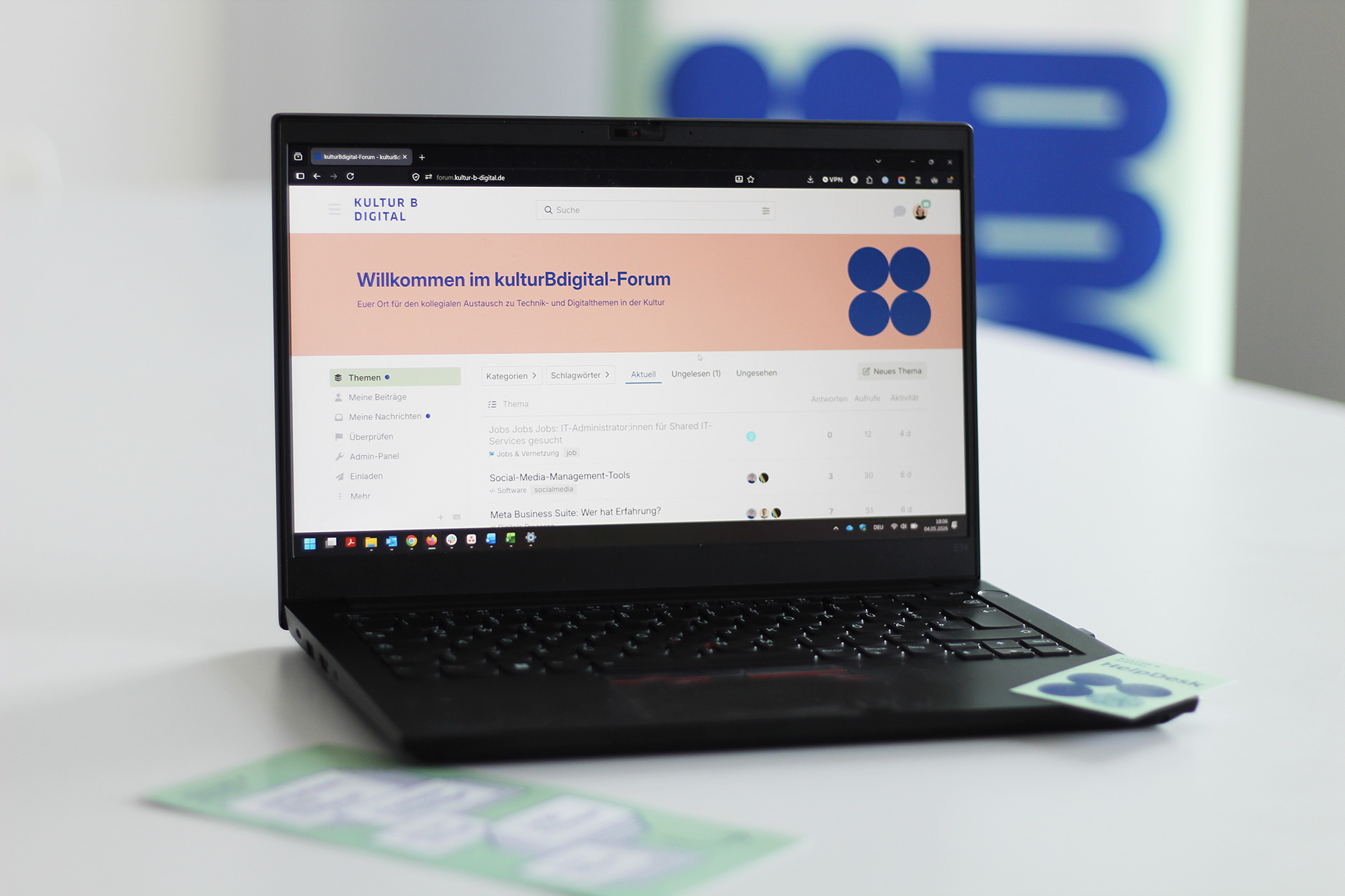 Geöffneter Laptop mit kulturBdigital-Forum auf dem Screen, im Hintergrund ein grünes Banner mit Logo von kulturBdigital