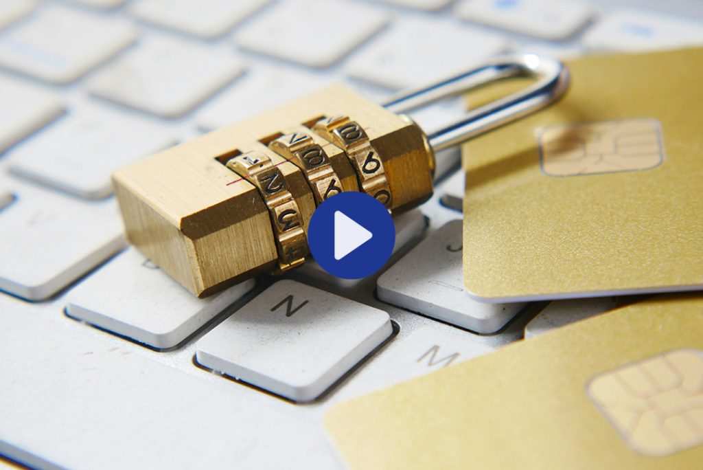 Nahaufnahme einer Computertastatur, auf der ein Zahlenschloss und mehrere Karten mit Sicherheits-Chips liegen. In der Mitte des Bildes signalisiert ein Play-Button, dass es sich um einen Video-Beitrag handelt.
