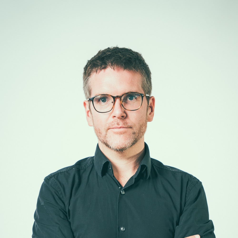 Porträt von Dieter Ripberger vor hellem Hintergrund, mit Brille, in dunklem Hemd