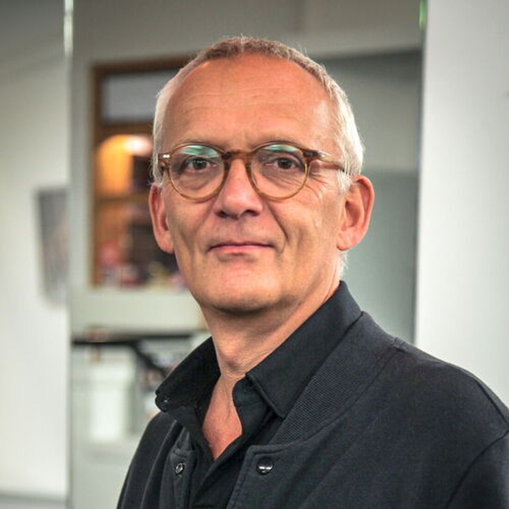 Porträt von Lars-Georg Vogel vor unscharfem Innenraum-Hintergrund, in dunklem Hemd.