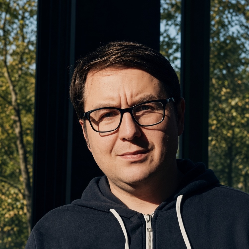Porträt von Marcel Karnapke im Freien vor Bäumen, in dunkler Kapuzenjacke.
